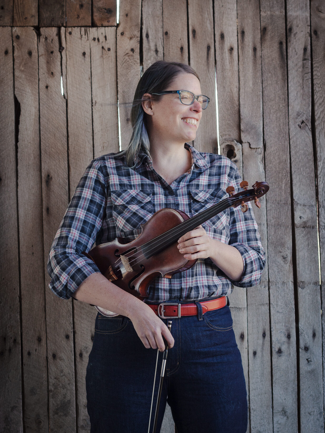 Stacey holding her fiddle while standing in front of a barn wall